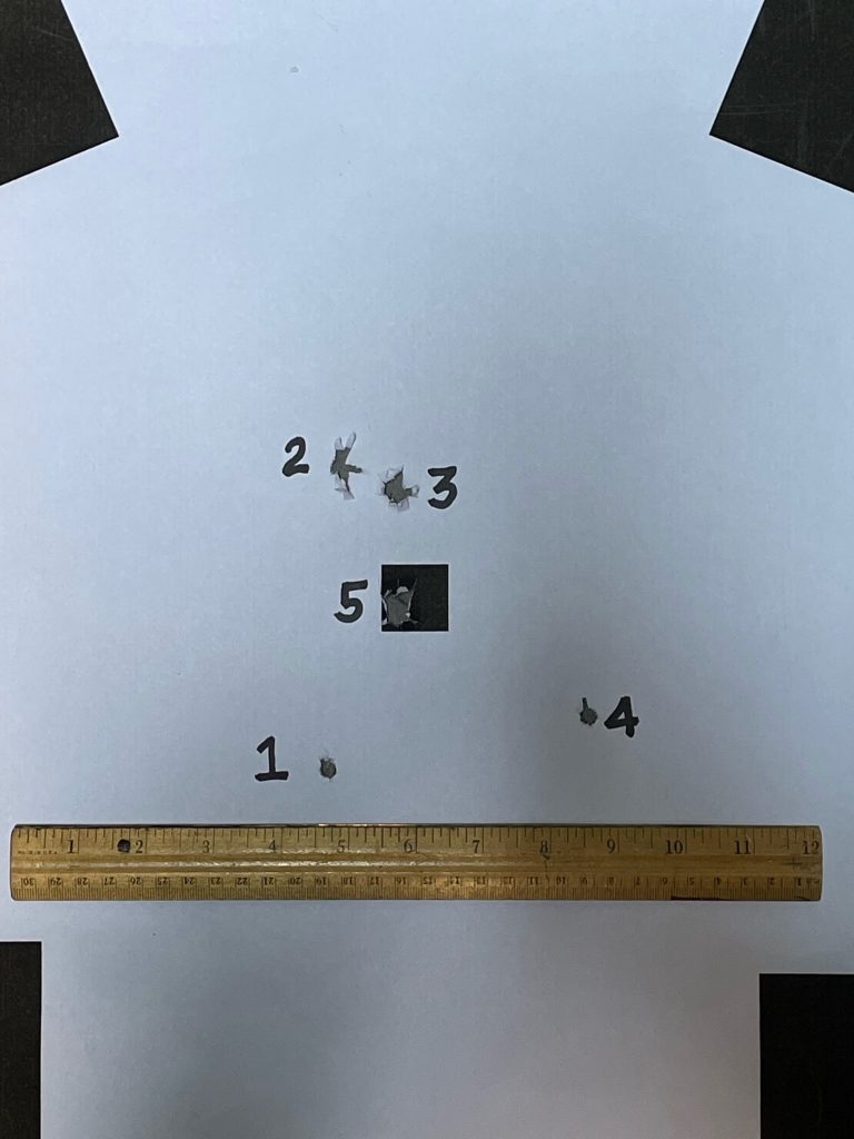 A target with 5 numbered bullet holes and ruler for scale